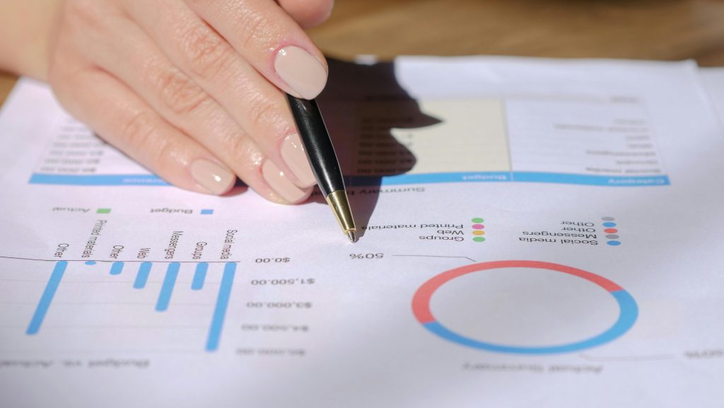 Close-up of a hand with a pen pointing at a financial document with graphs and charts.